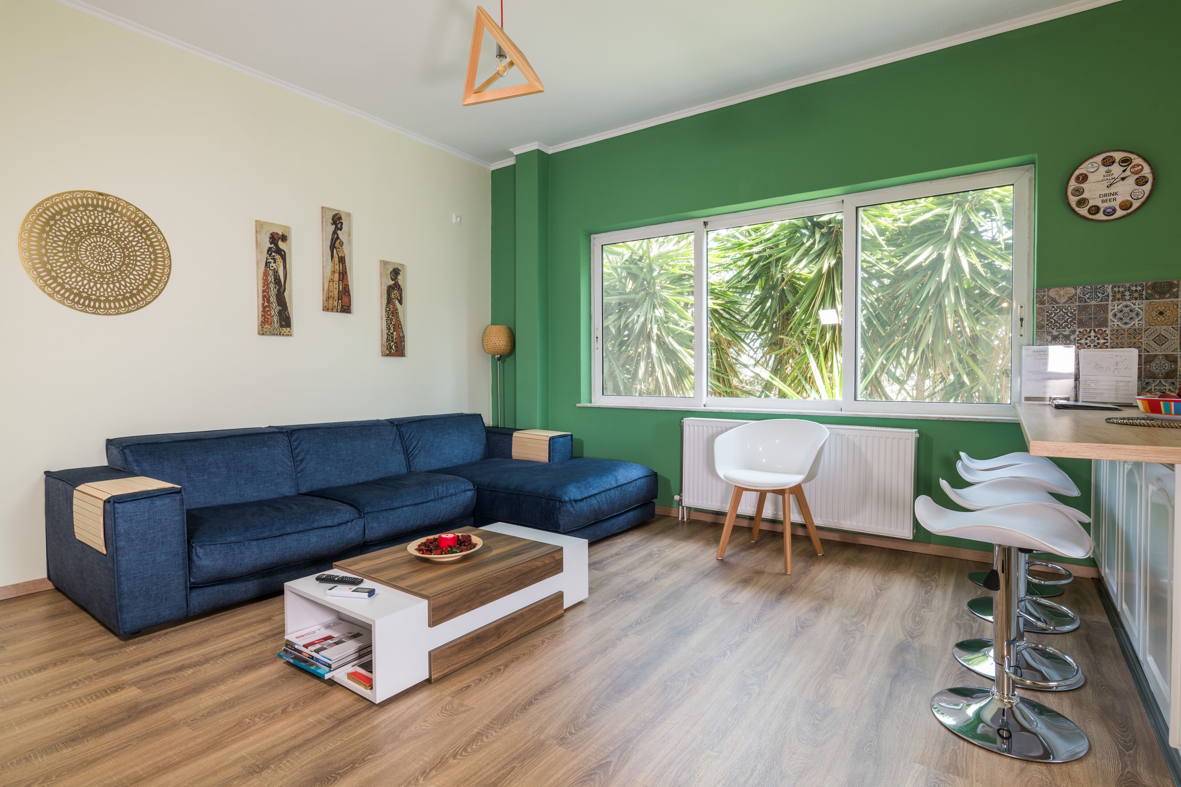 A modern living room with a blue sofa, a coffee table, and a white chair. There is a window with a view of palm trees.