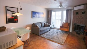 A living room with a gray sofa, a glass table, white chairs, a fireplace, and a ceiling fan. - Mt-Orford ski 8.5Km. Walk to old Magog! Lake view w/pools, hot tub, sauna! Quiet (Magog)