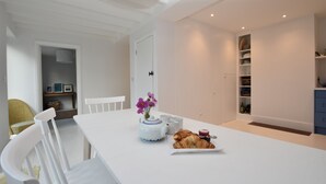 A modern dining area with a white table, chairs, a vase with flowers, and a croissant. - Seaside Retreat - Rye Harbour (Rye)