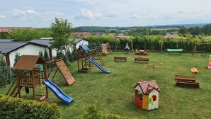 A playground with slides and climbing structures, surrounded by benches and a small house-like structure. - Holiday homes with terraces, close to the beach (Jaroslawiec)