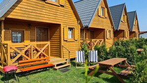 A row of wooden cabins with a grassy yard, picnic tables, and striped beach chairs. - Holiday homes with terraces, close to the beach (Jaroslawiec)