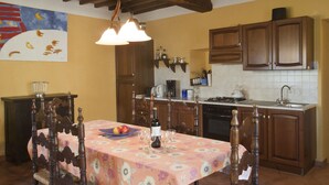 Un comedor con una mesa dispuesta para seis comensales, un cuadro en la pared, armarios de madera y una cocina al fondo.