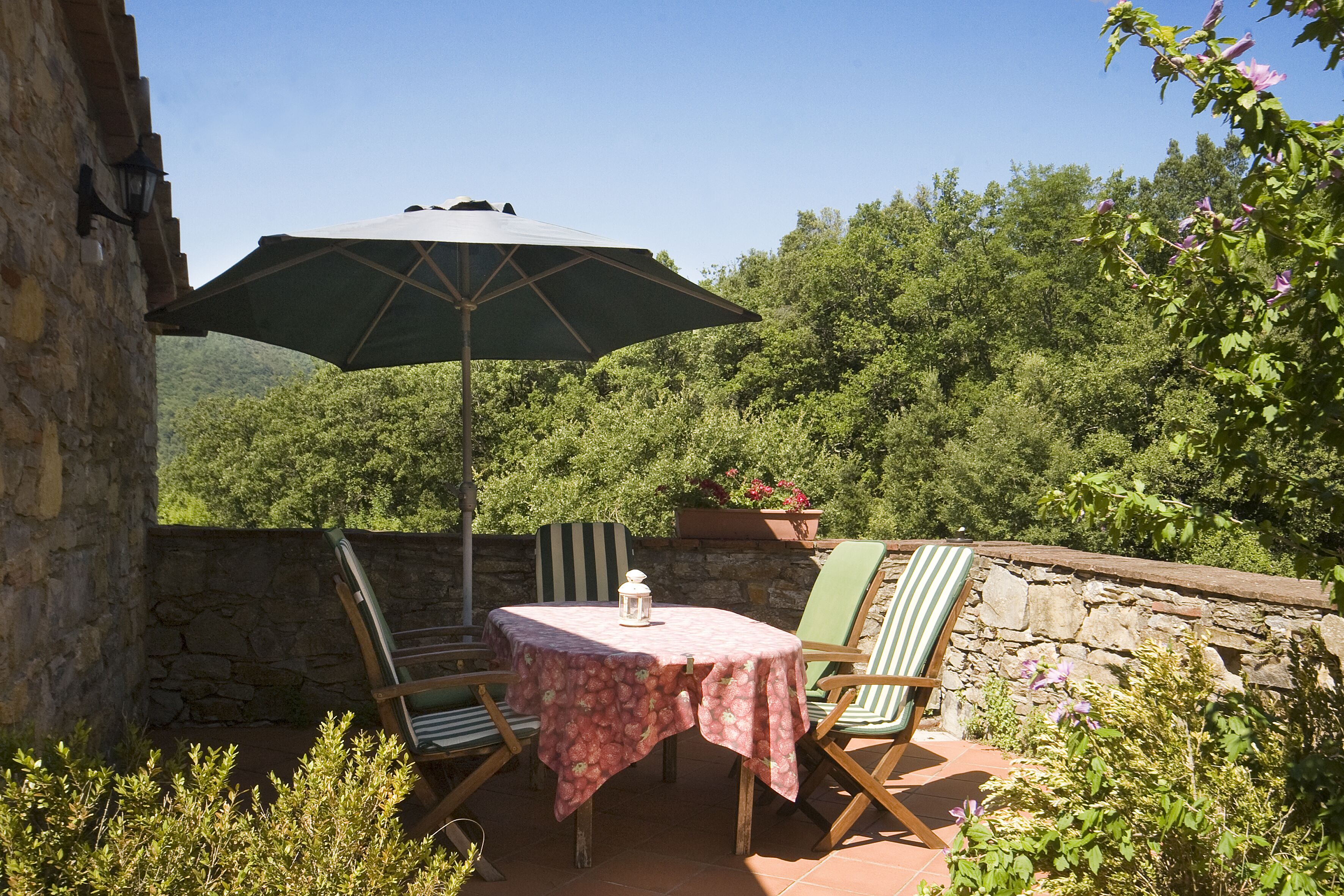 A patio with a table and chairs, an umbrella, and a stone wall.