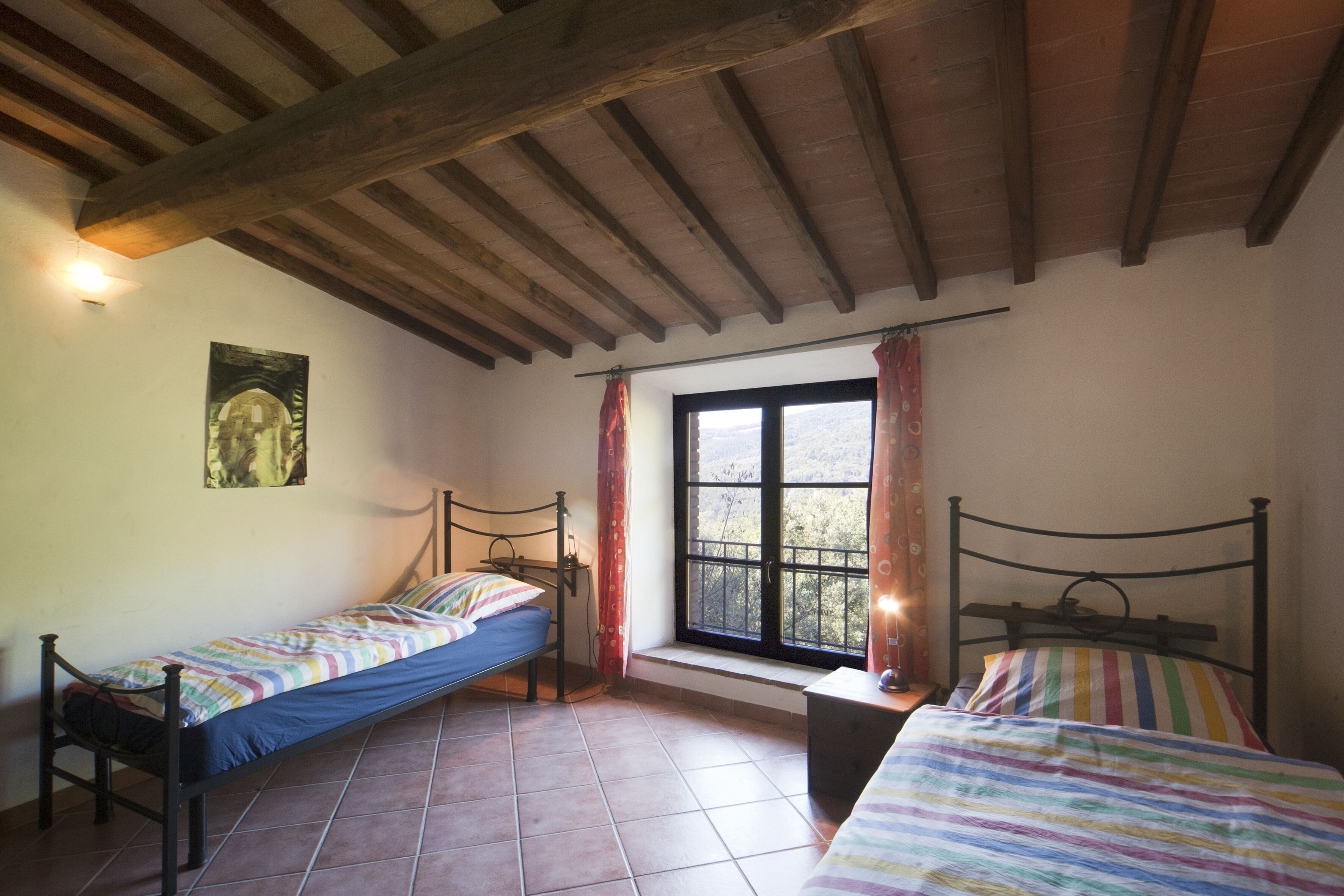 A bedroom with two single beds, a window with curtains, a painting on the wall, and a tiled floor.