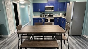 A kitchen with blue cabinets, a stainless steel refrigerator, and a wooden dining table with chairs. - Cheerful 3 Bed home w/ free parking, Wifi, Full Kitchen & Workstation. Sleeps 9 (Orlando)