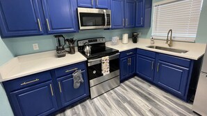 A kitchen with blue cabinets, stainless steel appliances, a white countertop, and a window with blinds. - Cheerful 3 Bed home w/ free parking, Wifi, Full Kitchen & Workstation. Sleeps 9 (Orlando)