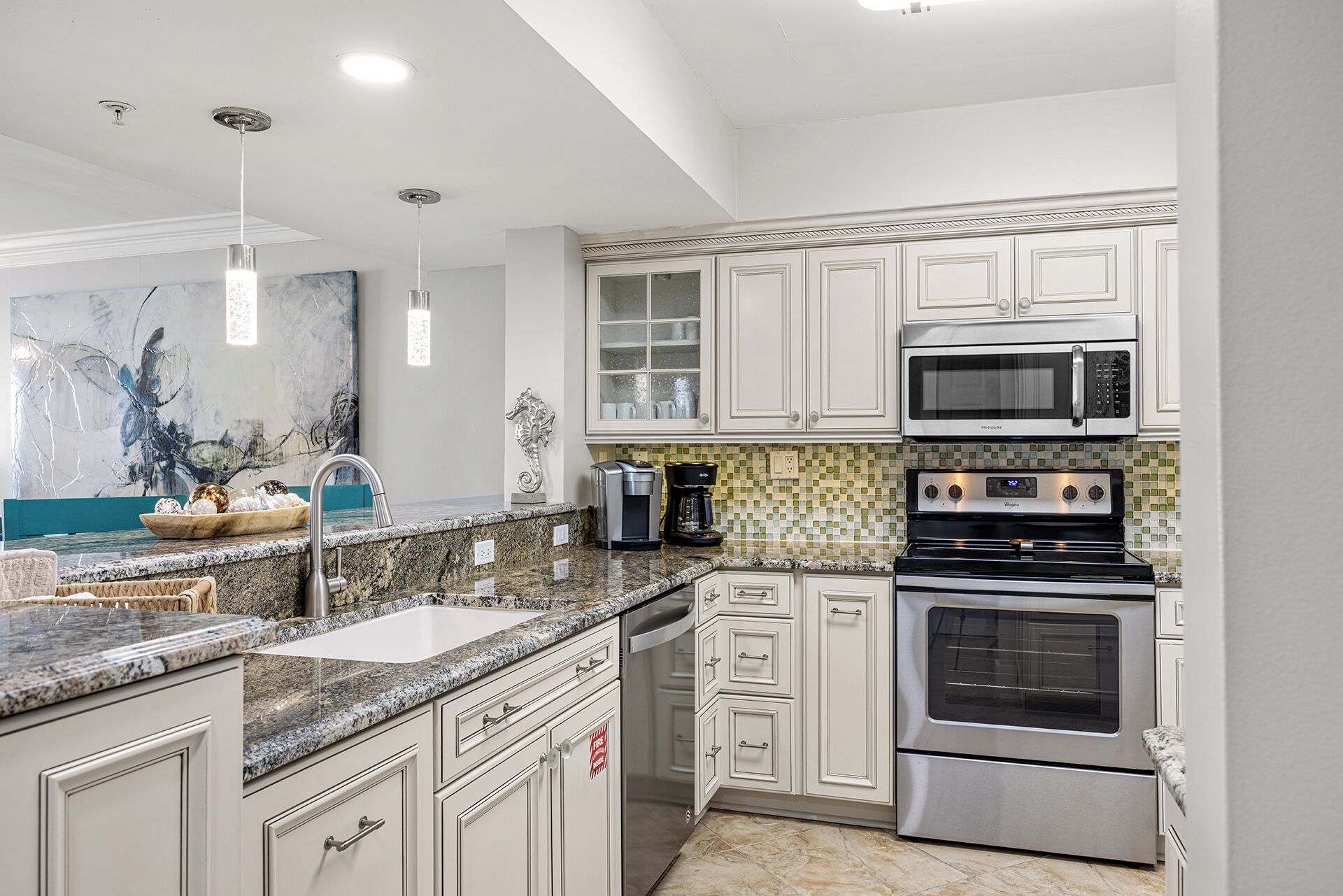 A kitchen with white cabinets, a granite countertop, a microwave, an oven, and a coffee maker.