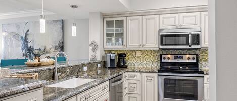 A kitchen with white cabinets, a granite countertop, a microwave, an oven, and a coffee maker.
