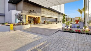 A modern building with a large entrance, a sign reading "Radisson," and a paved area with potted plants. - Radisson Hotel Nathdwara (Nathdwara)