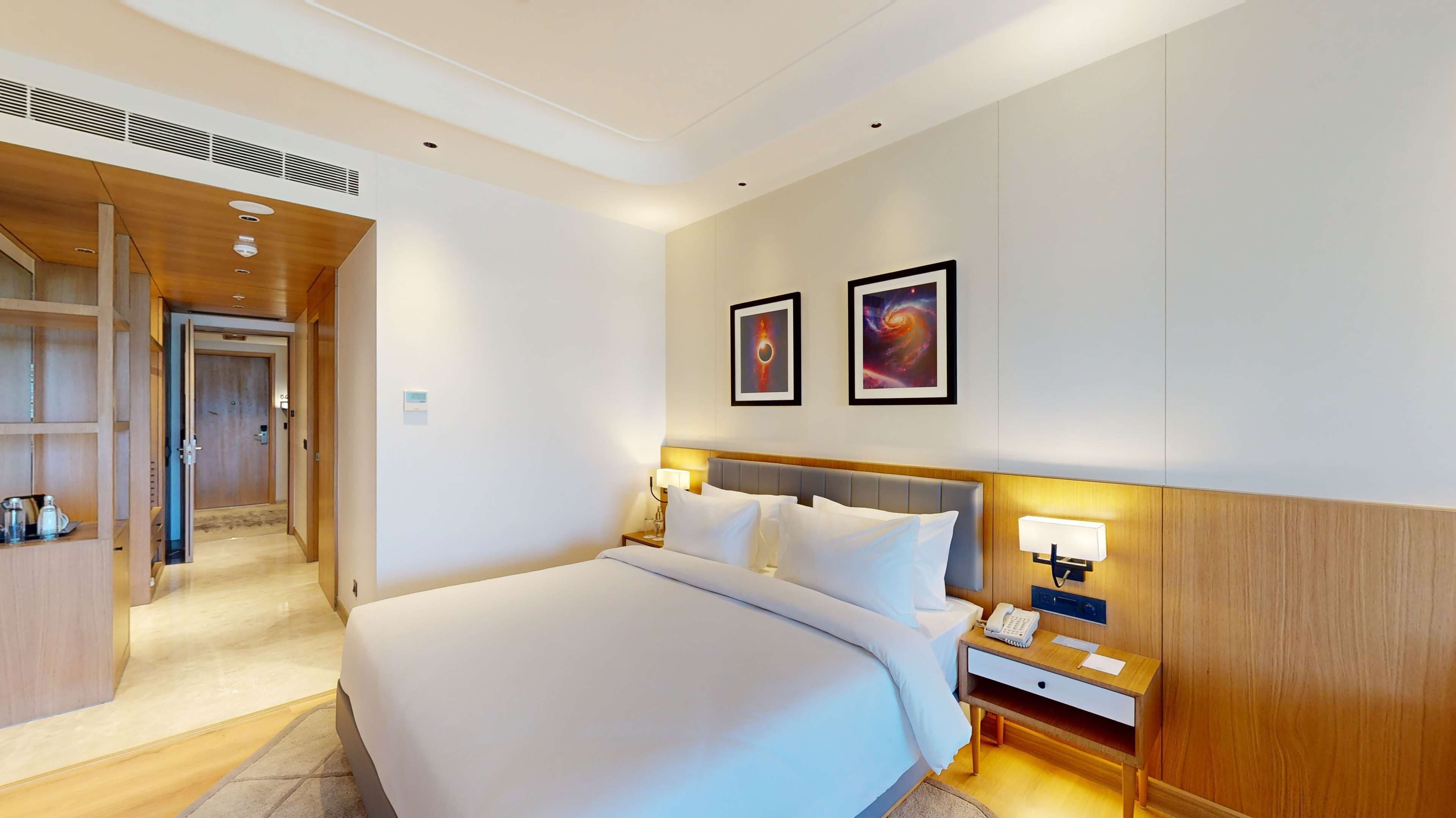 Una habitación de hotel con una cama grande, mesitas de noche, un armario y un pasillo que da a otra habitación.