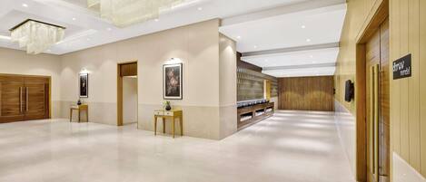 A spacious lobby with a polished marble floor, wooden paneling, and modern chandeliers.