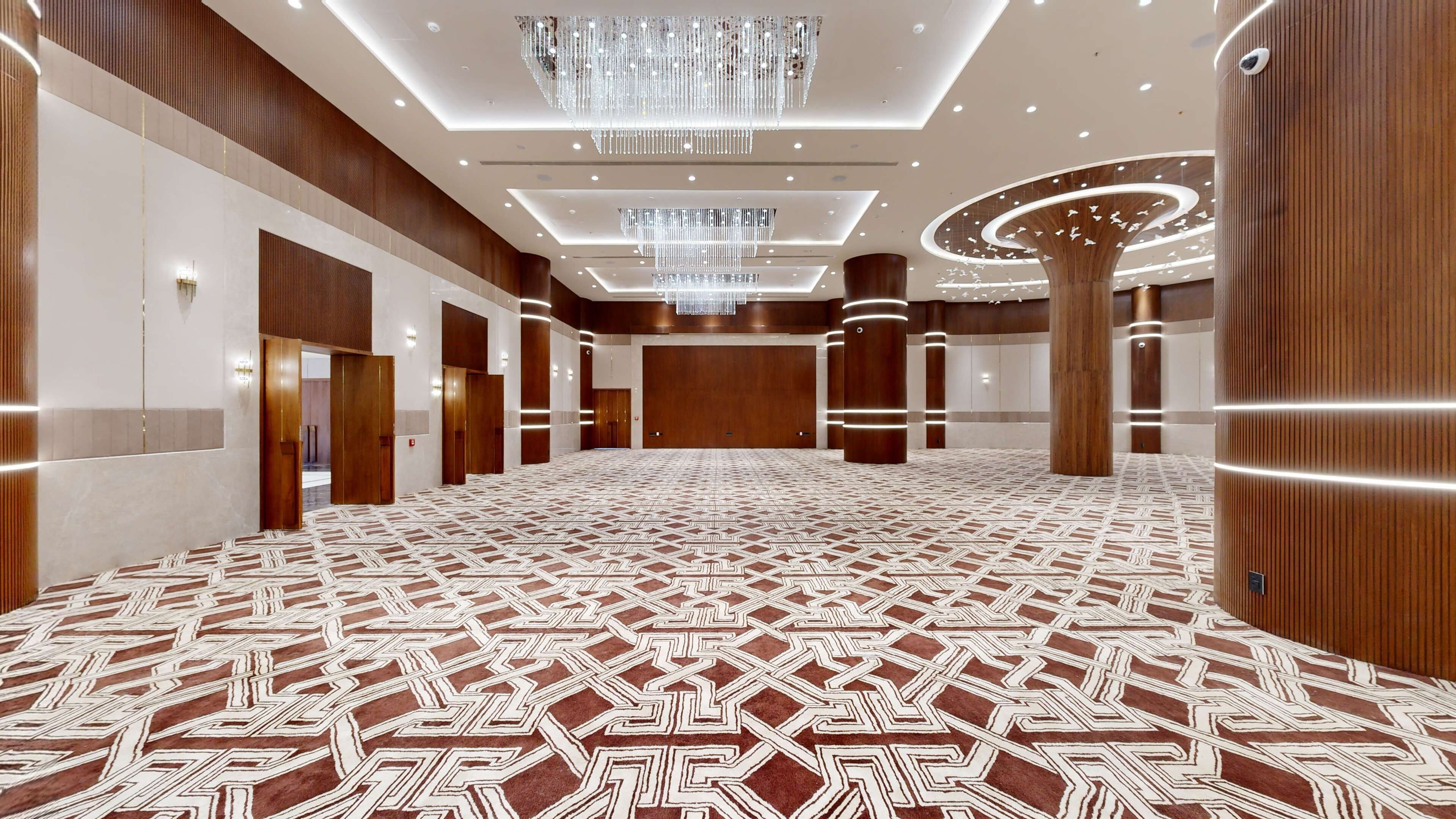 Un hall d’hôtel spacieux, doté d’un tapis à motifs, de lambris en bois et d’un grand lustre.