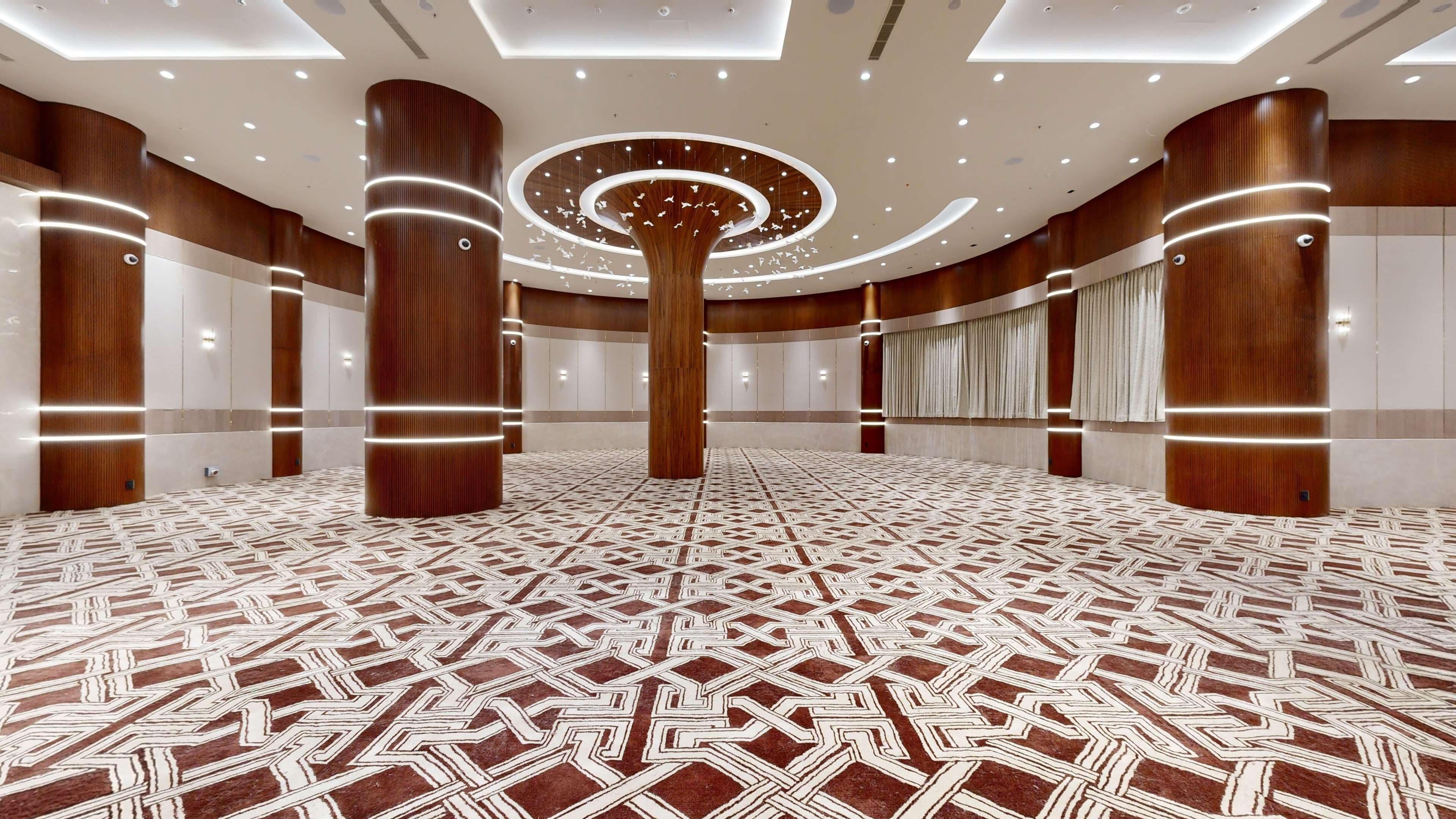 Een ruime, moderne hotel lobby met een geometrisch patroon tapijt, houten kolommen en inbouwverlichting.