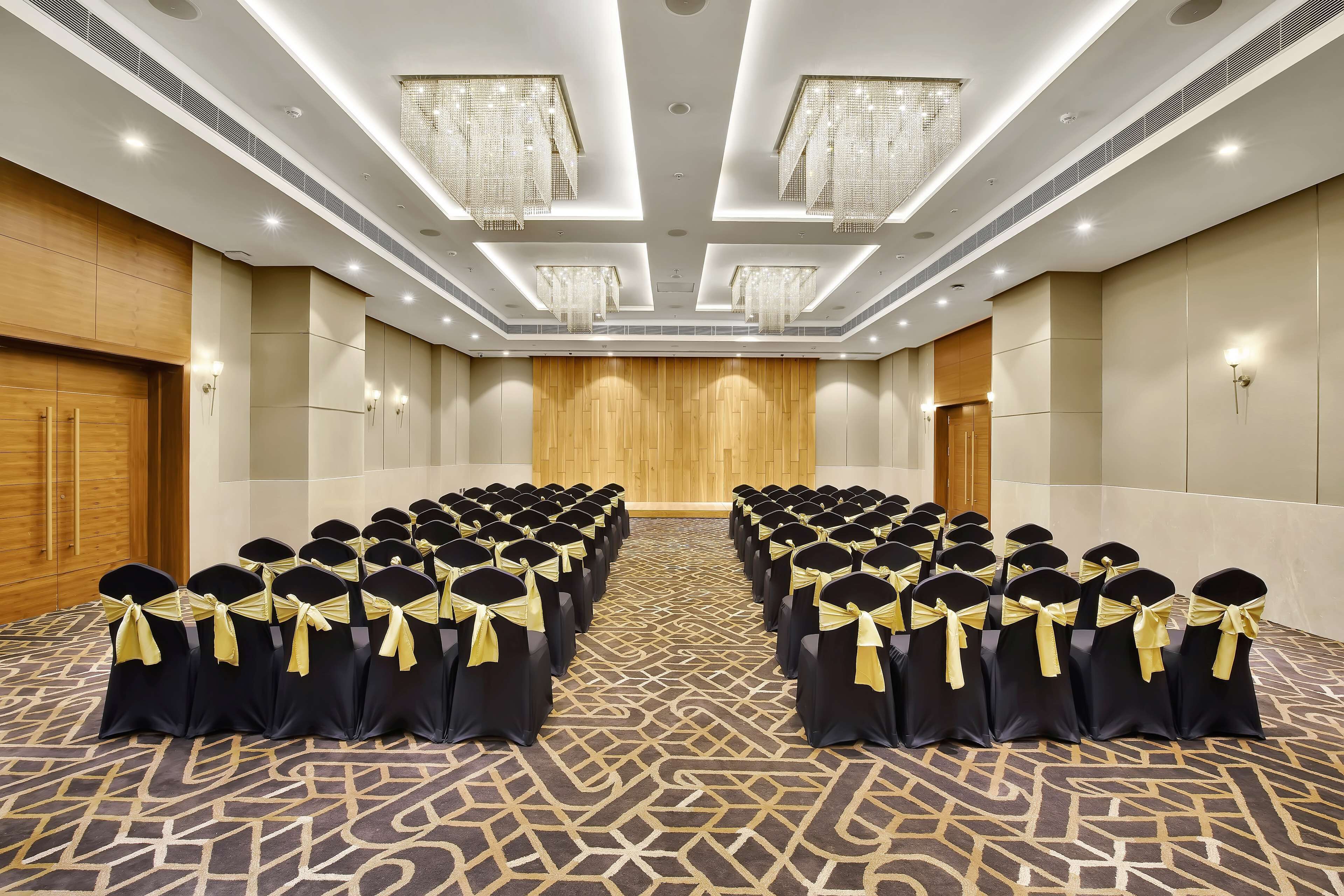 Een congreszaal met rijen stoelen, een wand van houten panelen en kroonluchters.
