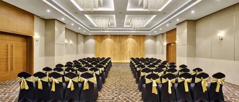 A conference room with rows of chairs, a wooden panel wall, and chandeliers.