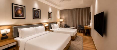A hotel room with two beds, a desk, a chair, a television, and artwork on the walls.