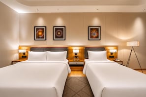 A hotel room with two beds, a nightstand with a lamp, a floor lamp, and three framed artworks on the wall. - Radisson Hotel Nathdwara (Nathdwara)