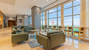A spacious lobby with a modern design, featuring a seating area with sofas and chairs, a coffee table, and a large window offering a view of the outdoors. - Radisson Hotel Nathdwara (Nathdwara)