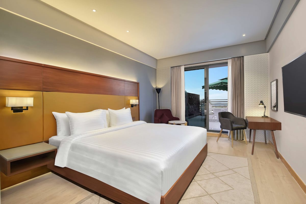 A hotel room with a large bed, a desk, a chair, and a view of the outside.