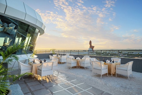A rooftop terrace with white wicker furniture and a view of the sea.