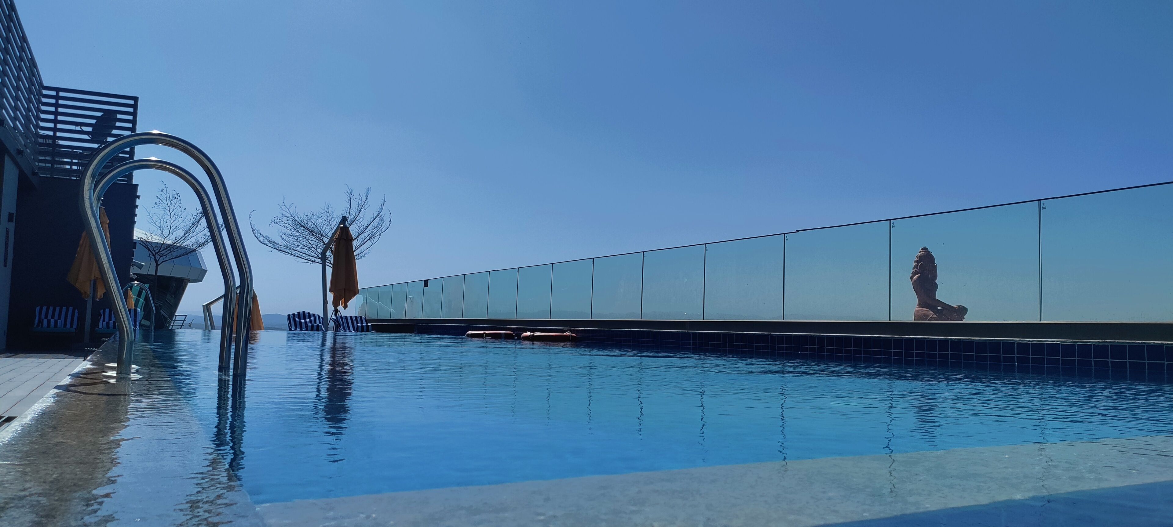 Una piscina moderna con un cielo azul despejado, una estructura metálica a la izquierda y una pared de azulejos a la derecha.