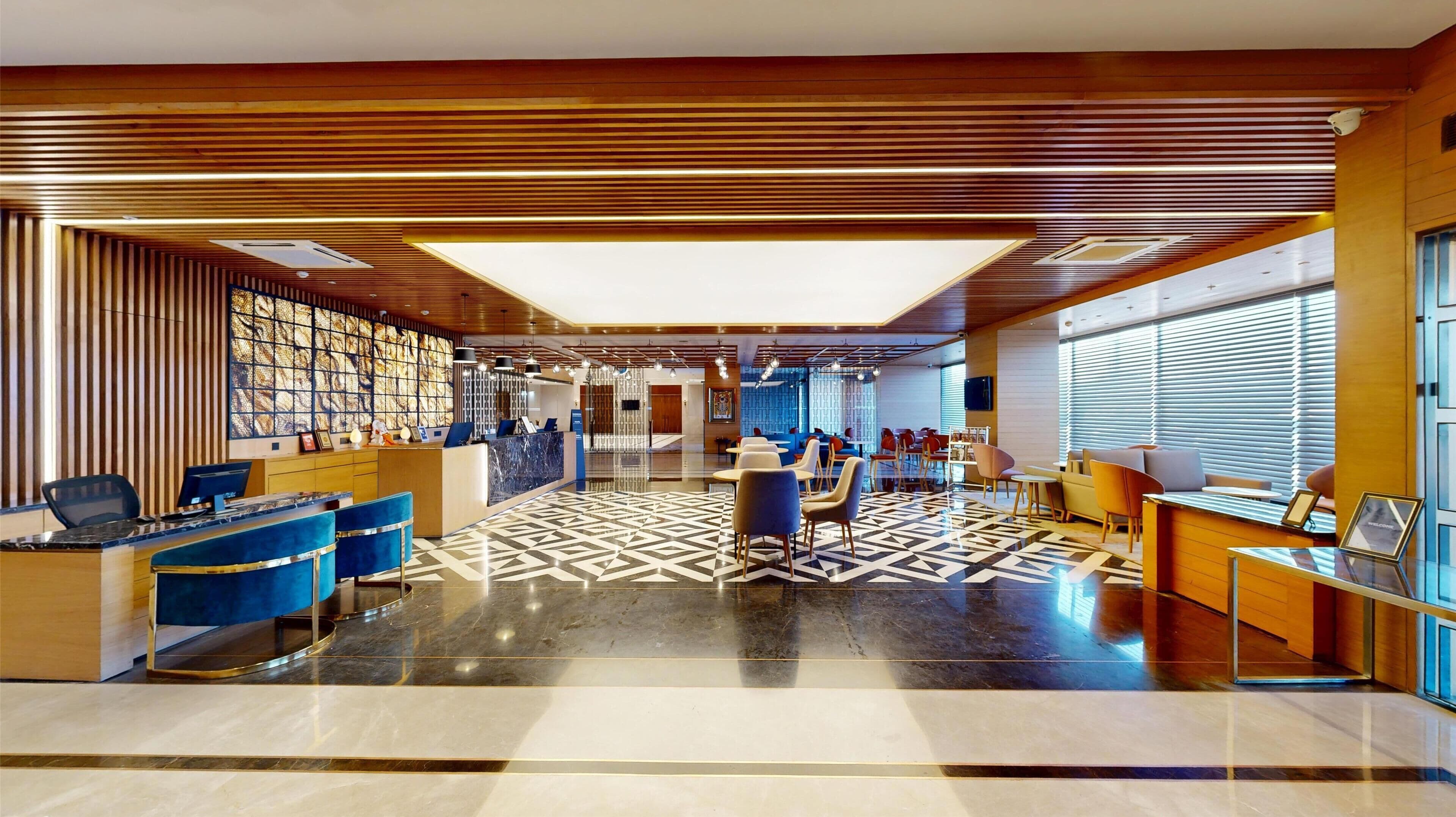 A modern hotel lobby with a reception desk, seating area, and a patterned floor.