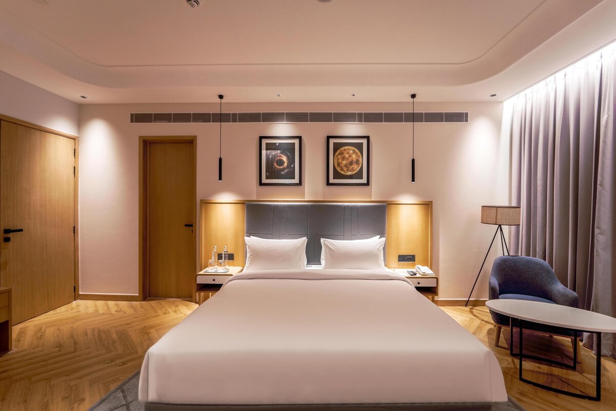 Una habitación de hotel con una cama grande, mesitas de noche, un escritorio, una silla y obras de arte en la pared.