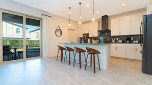 A modern kitchen with a central island, bar stools, and a large refrigerator. - Family Beach House near the Ocean (Melbourne Beach)