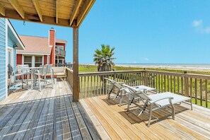 Une terrasse en bois avec des chaises longues blanches, une rambarde en bois et une vue sur la plage.
