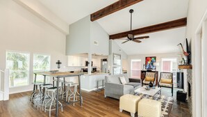 A spacious living area with a kitchen, wooden floors, a ceiling fan, and a fireplace. - Remodeled Beachfront Home w/ 2 decks & stellar Gulf views - Steps from Beach (Galveston)