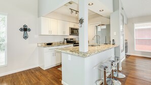 A modern kitchen with white cabinets, granite countertops, and a central island with bar stools. - Remodeled Beachfront Home w/ 2 decks & stellar Gulf views - Steps from Beach (Galveston)