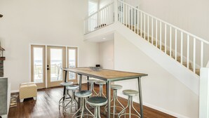 A spacious kitchen with a wooden table and bar stools, a staircase, and a view through glass doors. - Remodeled Beachfront Home w/ 2 decks & stellar Gulf views - Steps from Beach (Galveston)