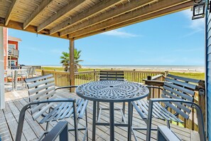 Une terrasse en bois avec une table et des chaises en métal, donnant sur une plage.