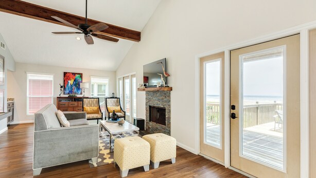 A spacious living room with a fireplace, a ceiling fan, and a large sliding glass door leading to a balcony. - Remodeled Beachfront Home w/ 2 decks & stellar Gulf views - Steps from Beach (Galveston)