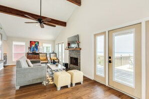 Un salon spacieux doté d’une cheminée, d’un ventilateur de plafond et d’une grande porte-fenêtre coulissante donnant sur un balcon.
