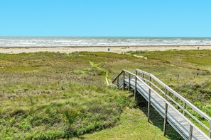 A wooden boardwalk leading to a beach with grassy dunes and a clear view of the ocean.