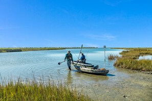 A calm water body with two people in a small boat, one standing and one seated, near the shore.
