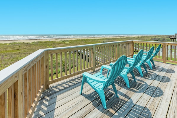 A wooden deck with turquoise chairs overlooking a beach.
