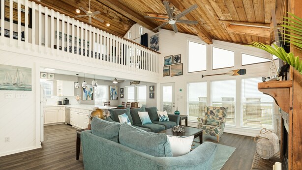 A spacious living area with a high ceiling, wooden beams, and a balcony with a railing. - Fresh Updates! Beachfront Escape w/ 2 Decks, Open Living Area - Steps from Beach (Galveston)
