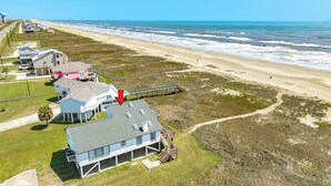 An aerial view of a coastal property with a beach, a pier, and a house with a staircase leading to a deck. - Fresh Updates! Beachfront Escape w/ 2 Decks, Open Living Area - Steps from Beach (Galveston)