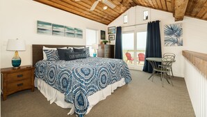 A bedroom with a large bed, a ceiling fan, a nightstand, a chair, and a view of the outside balcony. - Fresh Updates! Beachfront Escape w/ 2 Decks, Open Living Area - Steps from Beach (Galveston)