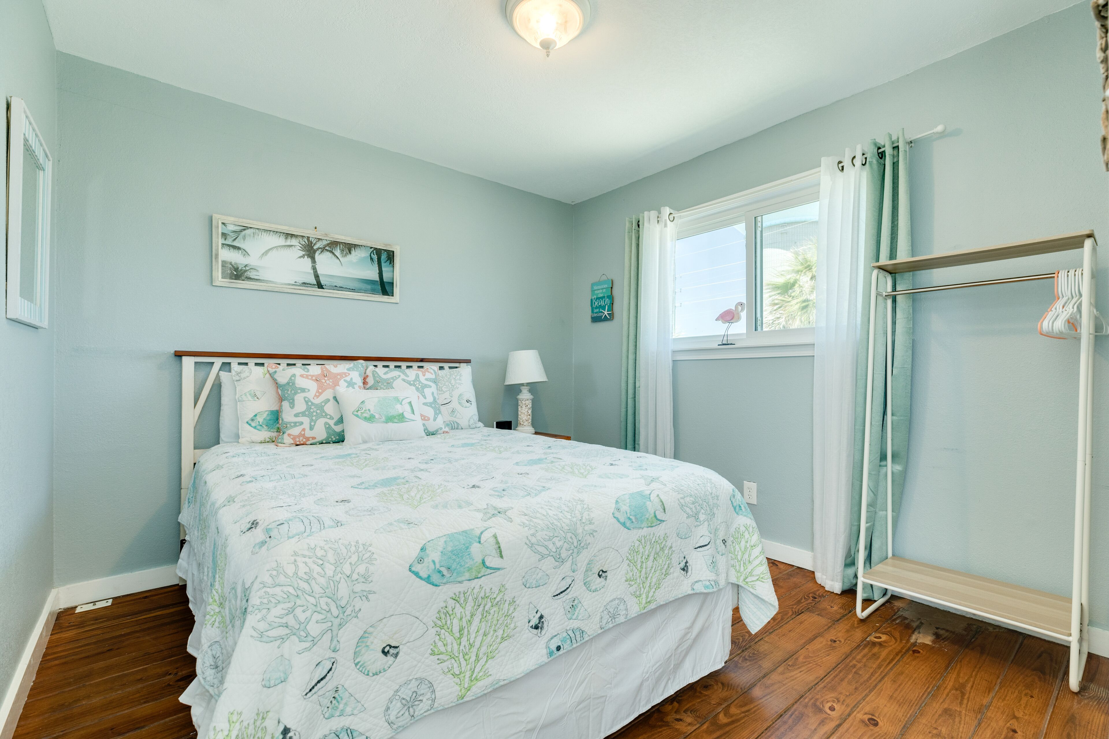 A bedroom with a bed, a nightstand, a window with curtains, and a wall-mounted shelf.