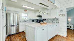 A modern kitchen with white cabinetry, a stainless steel refrigerator, and a large island with pendant lighting. - Budget & Pet Friendly Beachfront Home - Great for Couples or Small Families (Galveston)
