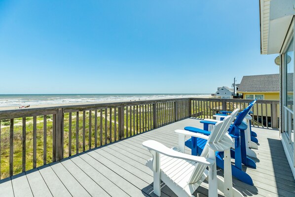 A wooden deck with white and blue Adirondack chairs overlooking a beach. - Private Beachfront Home - HOT TUB w/ Gulf Views, Steps from Beach & Dog Friendly (Galveston)