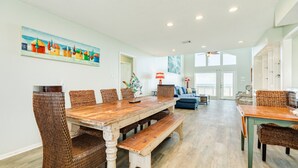 Un vaste espace dédié à la salle à manger, avec une table en bois et des chaises en osier, un canapé bleu et un tableau accroché au mur.