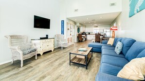 Un salon spacieux avec un canapé bleu, des fauteuils en osier, une table basse en bois et un téléviseur à écran plat fixé au mur.