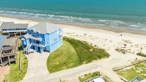 Un edificio grande azul con varios pisos y un balcón, ubicado en una playa con vista despejada al océano.
