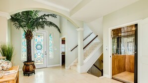 Un vestíbulo amplio con una palmera, una escalera y un ascensor de cristal.