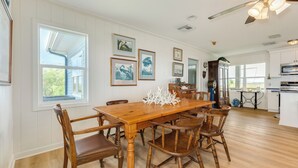 Un'ampia sala da pranzo con tavolo e sedie in legno, opere d'arte appese alle pareti e vista sulla cucina sullo sfondo.