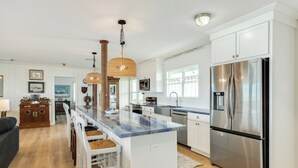 Una cucina moderna con mobili bianchi, un frigorifero in acciaio inossidabile e un'isola centrale con sgabelli da bar.